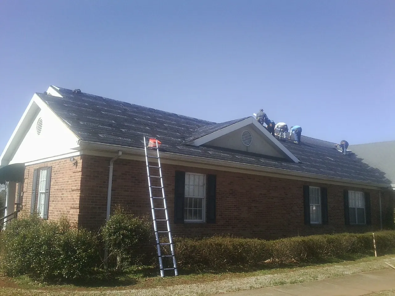Crew tearing shingles off a brick ranch roof with a ladder set — Emergency Roof Repair work by our crew in Gaines