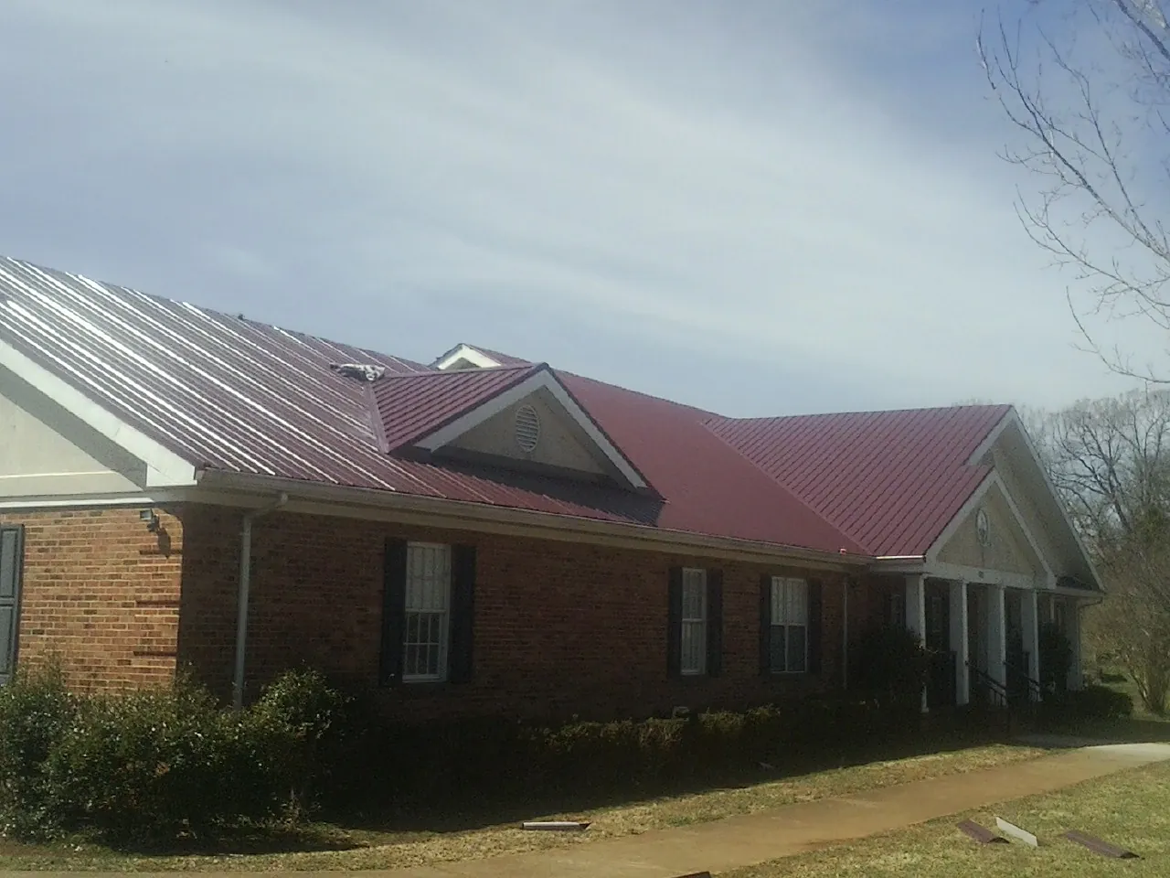 Red metal roof with gabled entries on a long brick building, from a Hail Damage Roof Repair job in Gaines