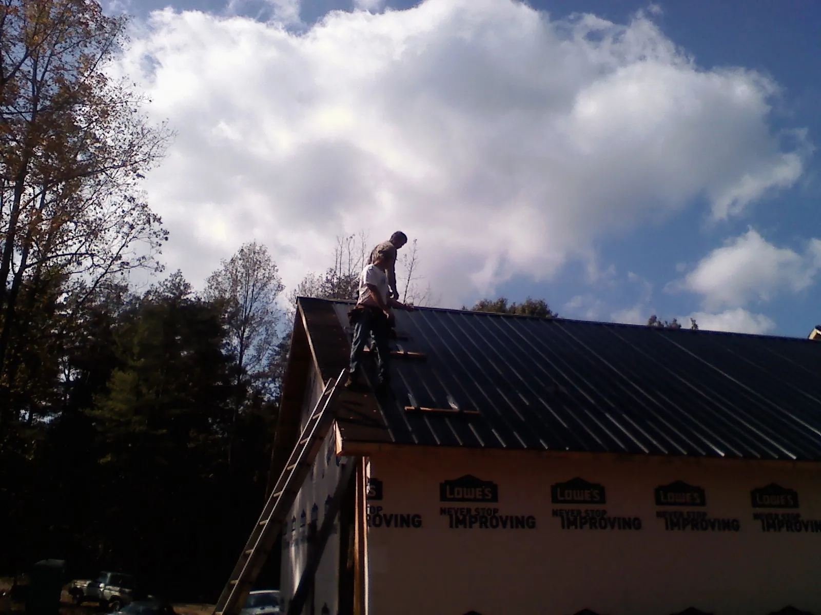Roofer fastening dark metal panels high against a cloudy sky, from a Roof Inspection job in Gaines