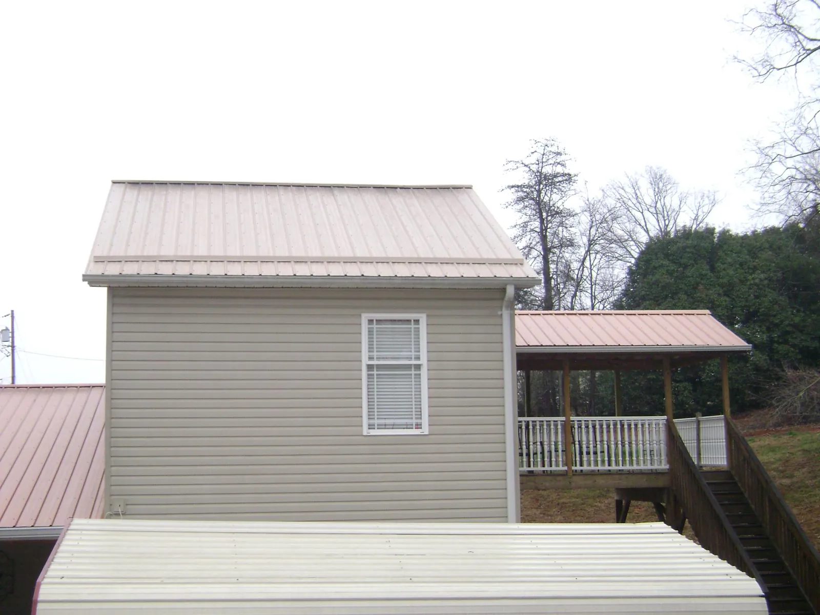 Tan metal roofs on a two story addition and attached porch, from a Roof Replacement job in Gaines